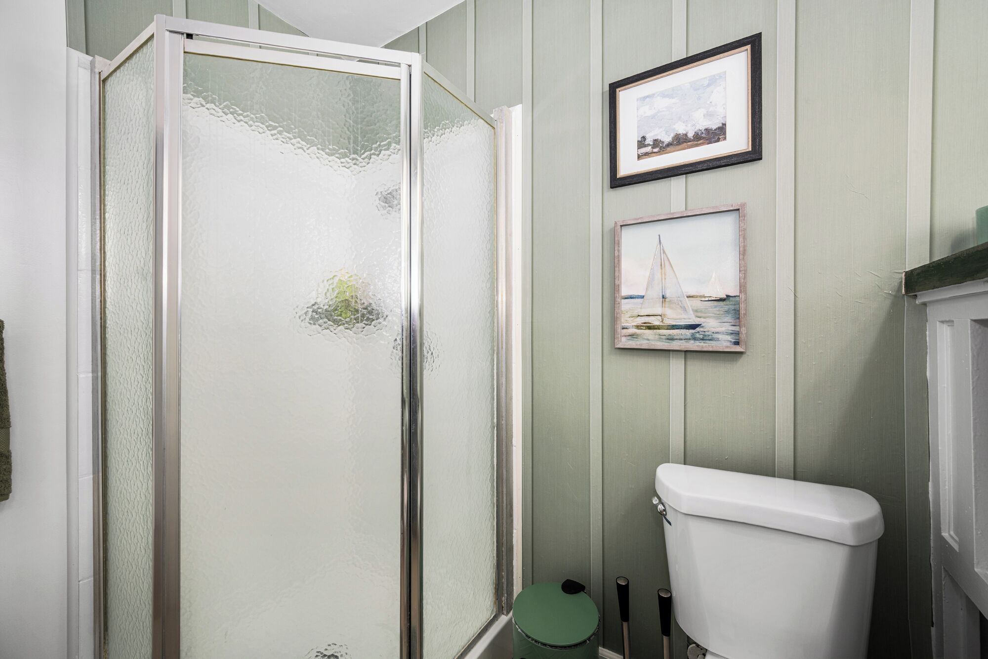 Un baño con cabina de ducha de vidrio, un inodoro y dos cuadros en la pared.