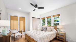Ein Schlafzimmer mit Bett, Nachttischen, Deckenventilator und Fenster mit Jalousien.