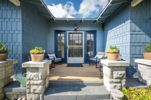 Une terrasse couverte avec deux chaises et des plantes en pot, une porte bleue et un mur en pierre.