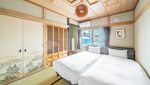 Et traditionelt japansk soveværelse med tatamimåtter, en stor seng med hvidt sengetøj, en shoji-skydedør og en loftsvifte.