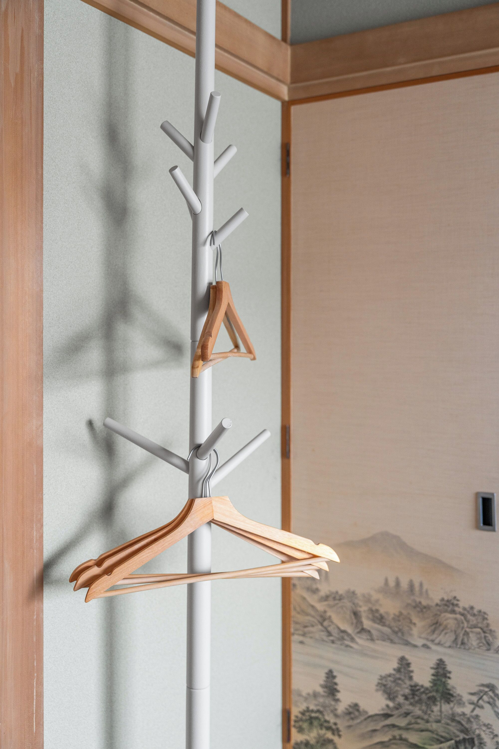 A wall-mounted coat rack with multiple hooks and wooden hangers against a wall with a traditional landscape painting.