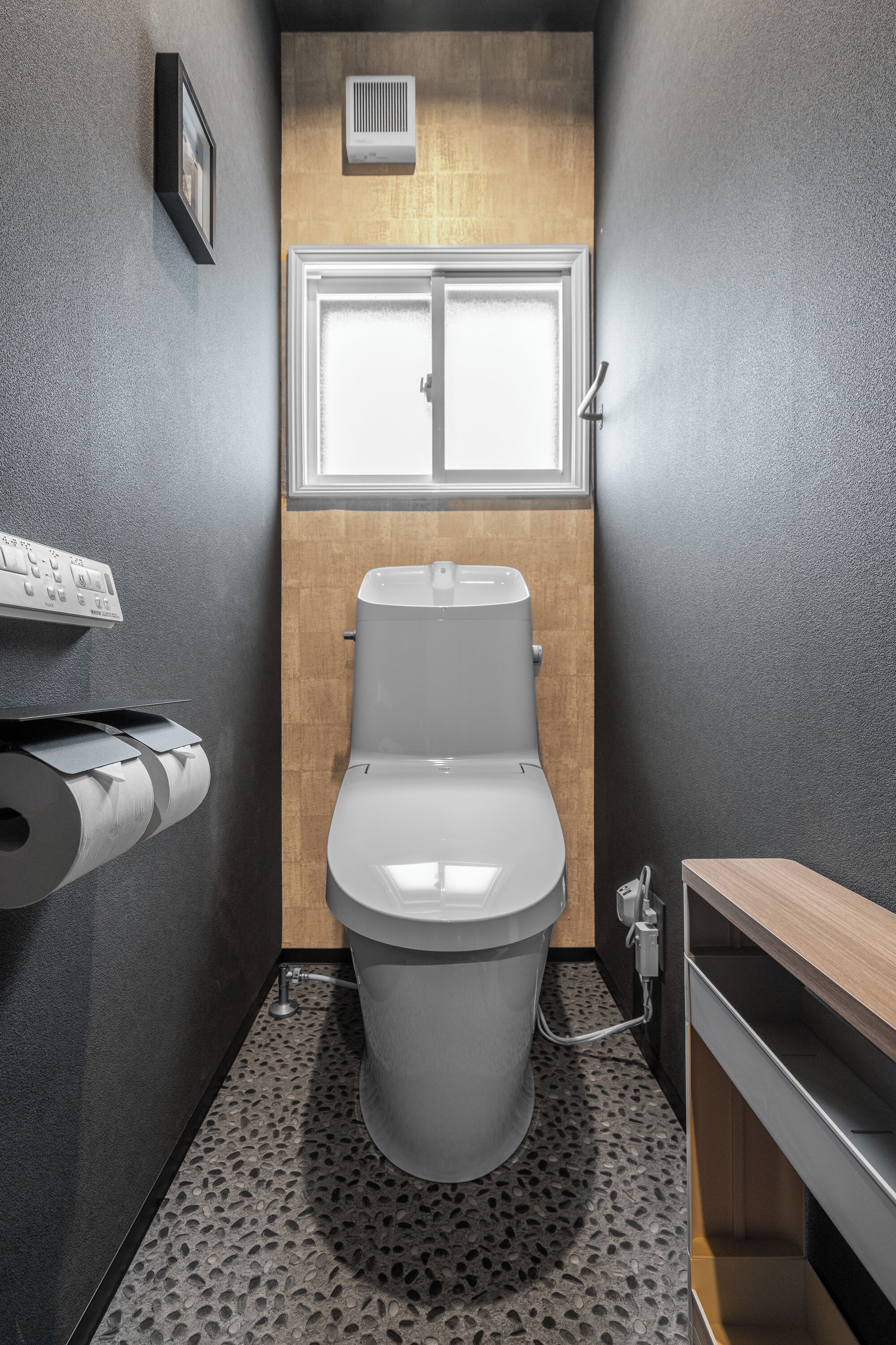 Une petite salle de bain comprenant des toilettes, un porte-rouleau de papier toilette, une fenêtre et un panneau en bois au-dessus des toilettes.