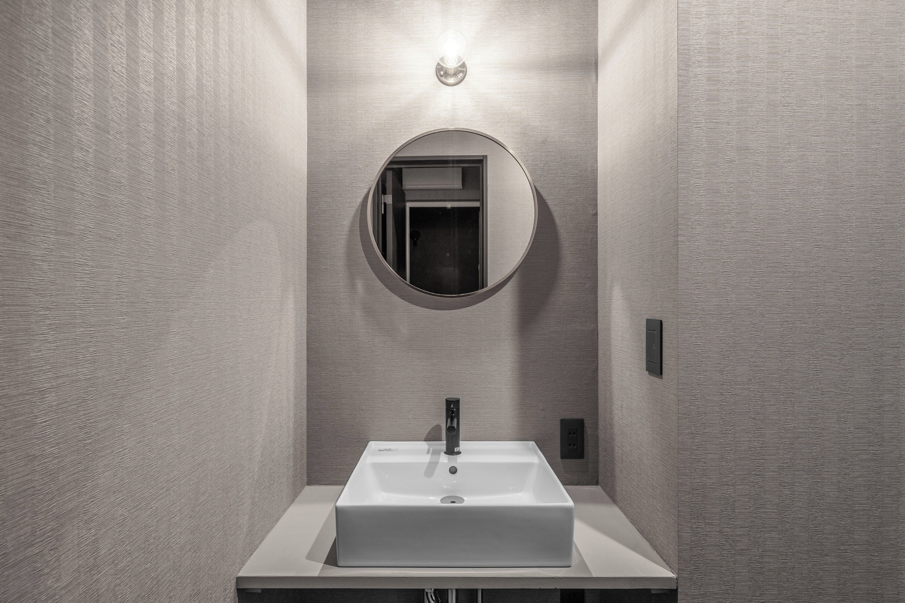 A modern bathroom with a rectangular sink, a round mirror, and a light fixture above the mirror.