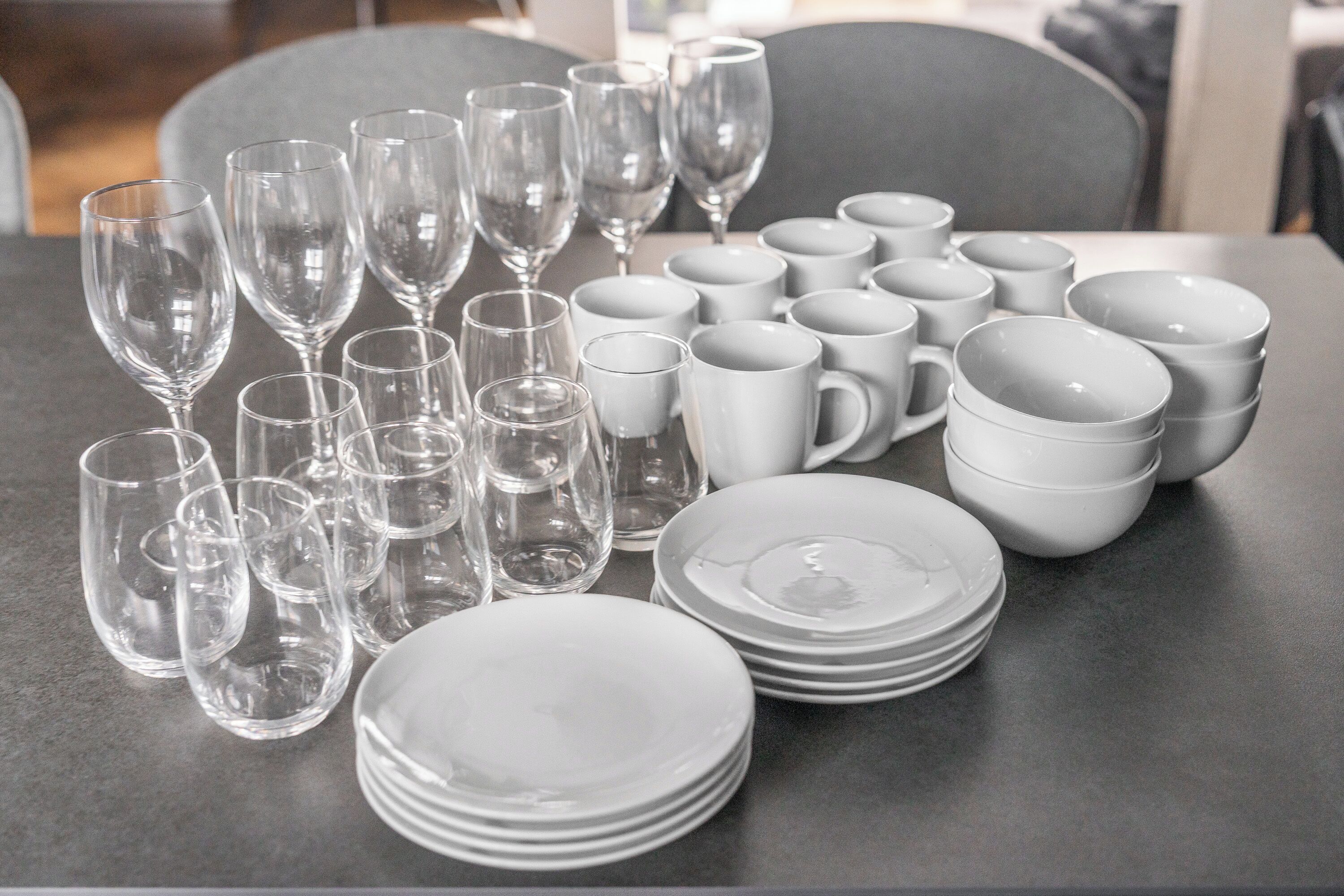 A table with stacks of white plates and clear wine glasses.