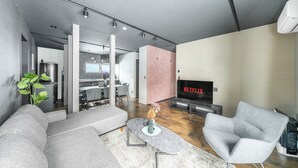 En moderne stue med en grå sofa, en grå lænestol og et marmorbord. Et fladskærms-tv er monteret på væggen med Netflix-logoet.