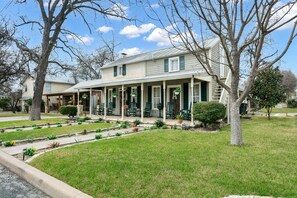 A two-story house with a covered porch, green shutters, and a well-maintained lawn. - Amoroso Cottage | 3/2.5, Full Kitchen, Fire-pit & Grill (Fredericksburg)