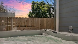 Un bain à remous entouré d’une clôture en bois, avec un verre de vin en arrière-plan.