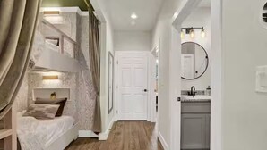 Une chambre à coucher comprenant un lit, une table de chevet et une commode. Une porte donne accès à une salle de bain équipée d’un lavabo et d’un miroir.