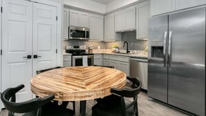 Une cuisine moderne avec des meubles gris, un réfrigérateur en acier inoxydable, un four à micro-ondes et une table à manger en bois avec des chaises.