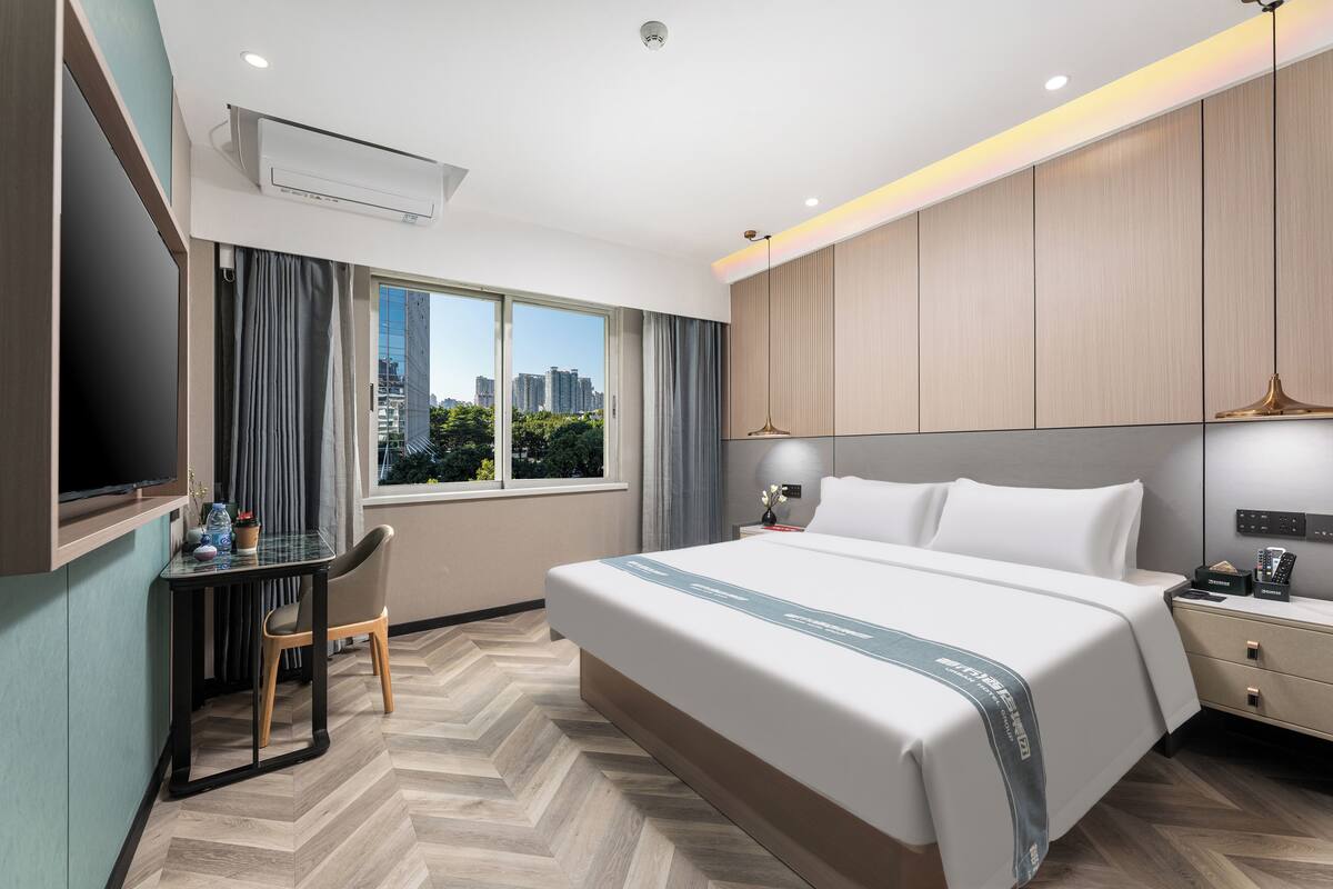 Una habitación de hotel con una cama grande, un escritorio con una silla, un televisor y una ventana con vista a la ciudad.