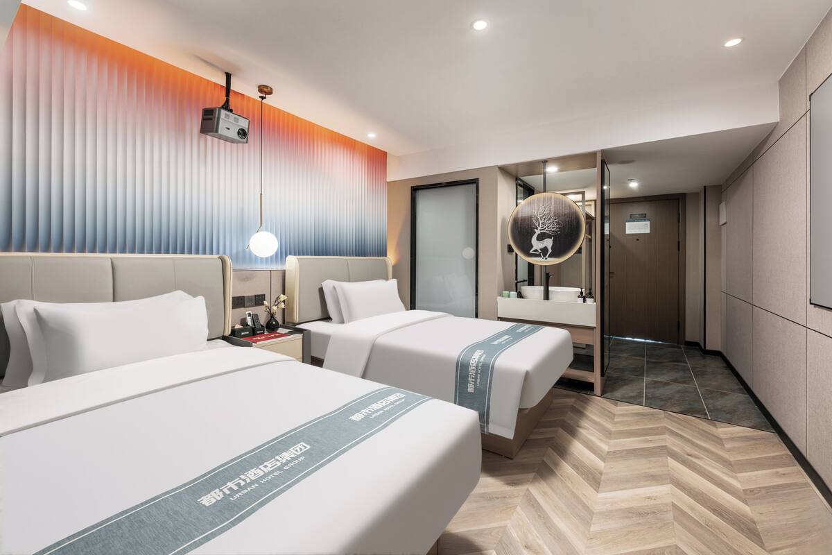 Habitación de hotel con dos camas, un espejo grande, un proyector en el techo y suelo con motivo de espiga.
