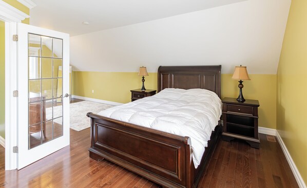 A bedroom with a wooden bed, two nightstands with lamps, a door with glass panels, and a carpeted floor.