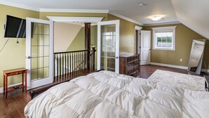 Ein Schlafzimmer mit einem großen Bett, einem Schminktisch, einem an der Wand befestigten Fernseher und einem Fenster mit Blick.
