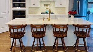 A kitchen with white cabinets, a central island with bar stools, stainless steel appliances, and pendant lighting.