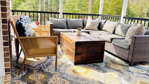 A covered outdoor seating area with a patterned rug, wicker furniture, and a view of trees.