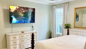 A bedroom with a large bed, a television mounted on the wall, a dresser, and a chandelier.