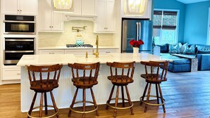 A modern kitchen with white cabinets, a central island with bar stools, stainless steel appliances, and pendant lighting.