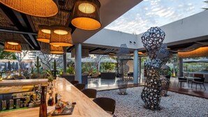 An outdoor dining area with a wooden table, wicker hanging lights, and decorative metal sculptures. - The Club at Solaz (San José del Cabo)