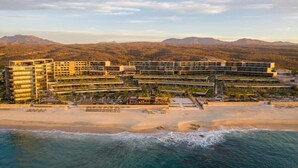 A beachfront hotel with multiple buildings, a sandy beach, and mountains in the background. - The Club at Solaz (San José del Cabo)