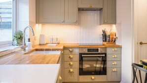 Een moderne keuken met grijze kastjes, een roestvrijstalen oven, een inbouwmagnetron en een raam dat natuurlijk licht binnenlaat.