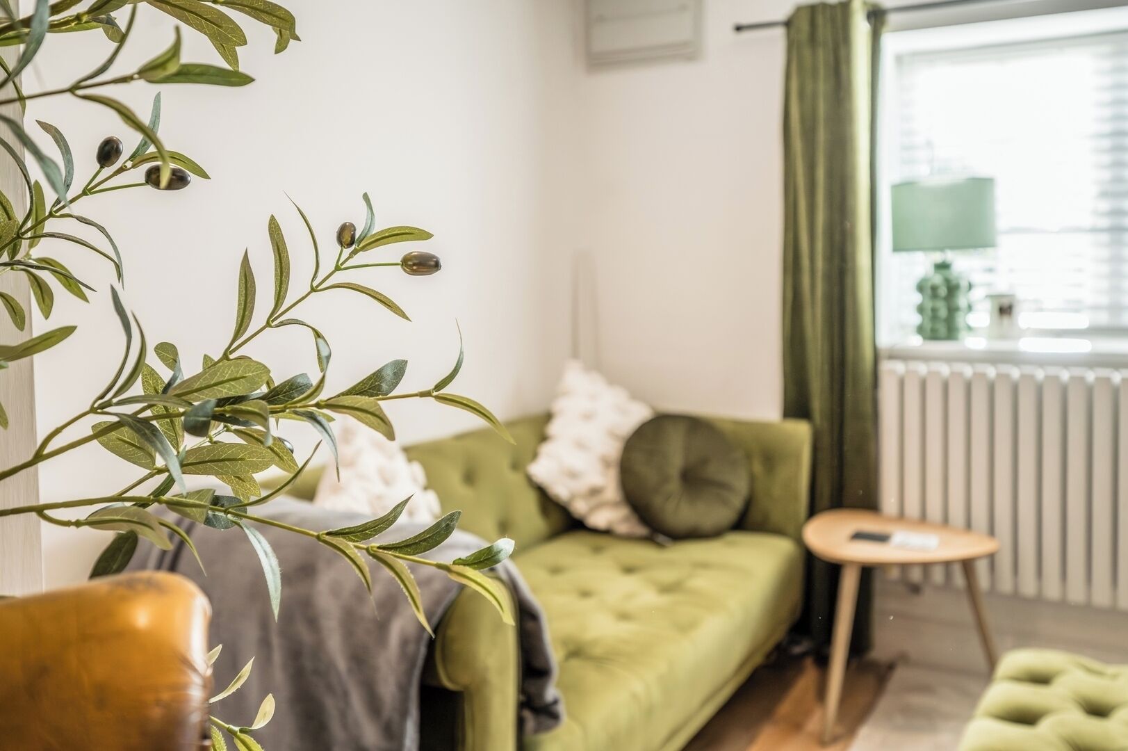 Una sala de estar acogedora con un sofá verde, una mesita redonda y una planta.