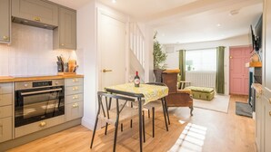 Een moderne keuken met een inbouwoven, een eethoek met tafel en stoelen, en een trap naar een woonruimte met een bank en een raam.