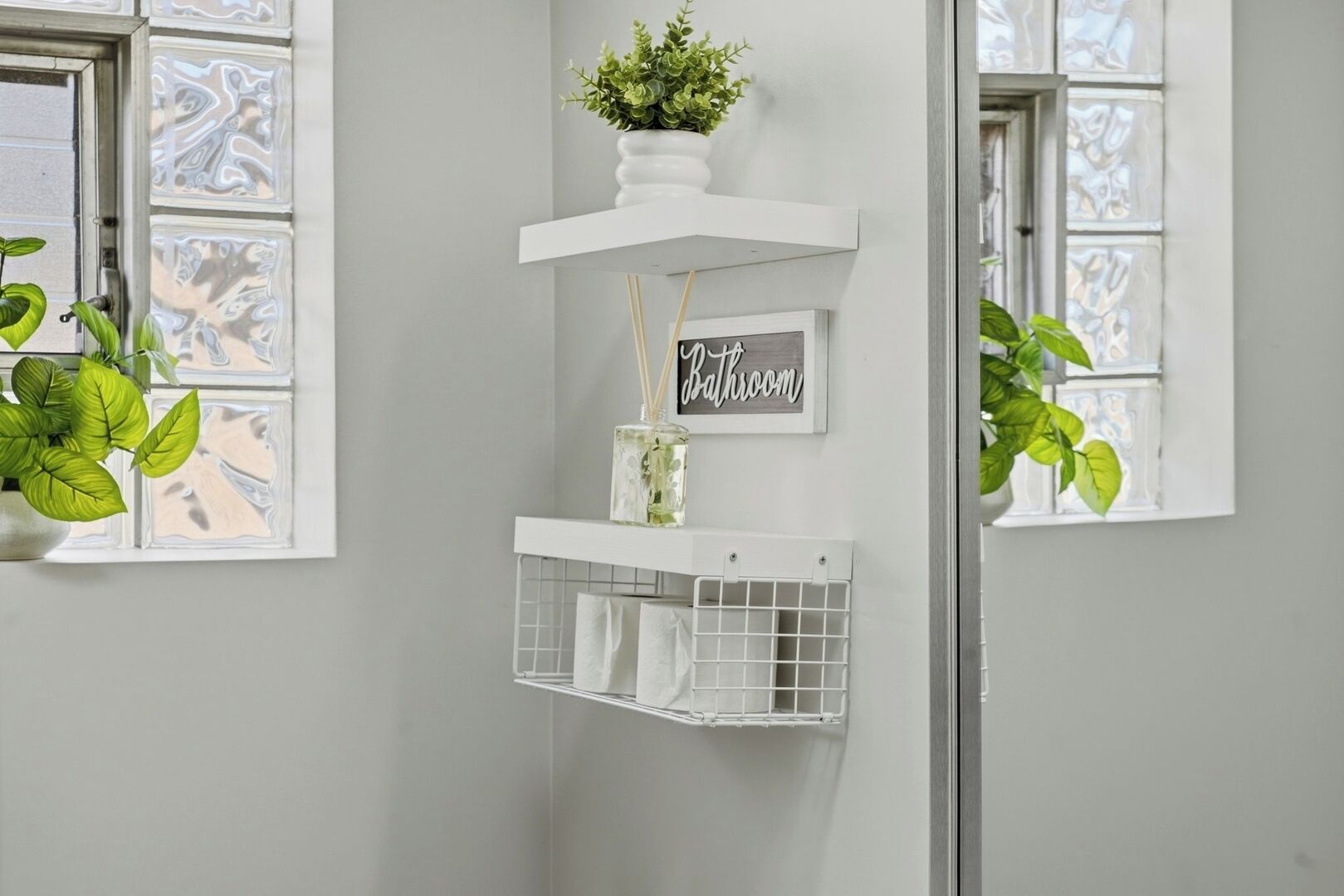 Un baño con un estante blanco que sostiene una planta, un letrero y un dispensador de pañuelos.