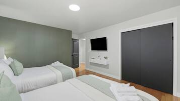 A modern hotel room with two beds, a TV mounted on the wall, a dark door, and a white console table.