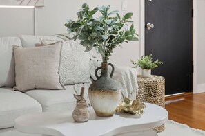 A living room with a white sofa, a decorative vase with a plant, a small wooden figurine, and a gold decorative piece on a white coffee table.