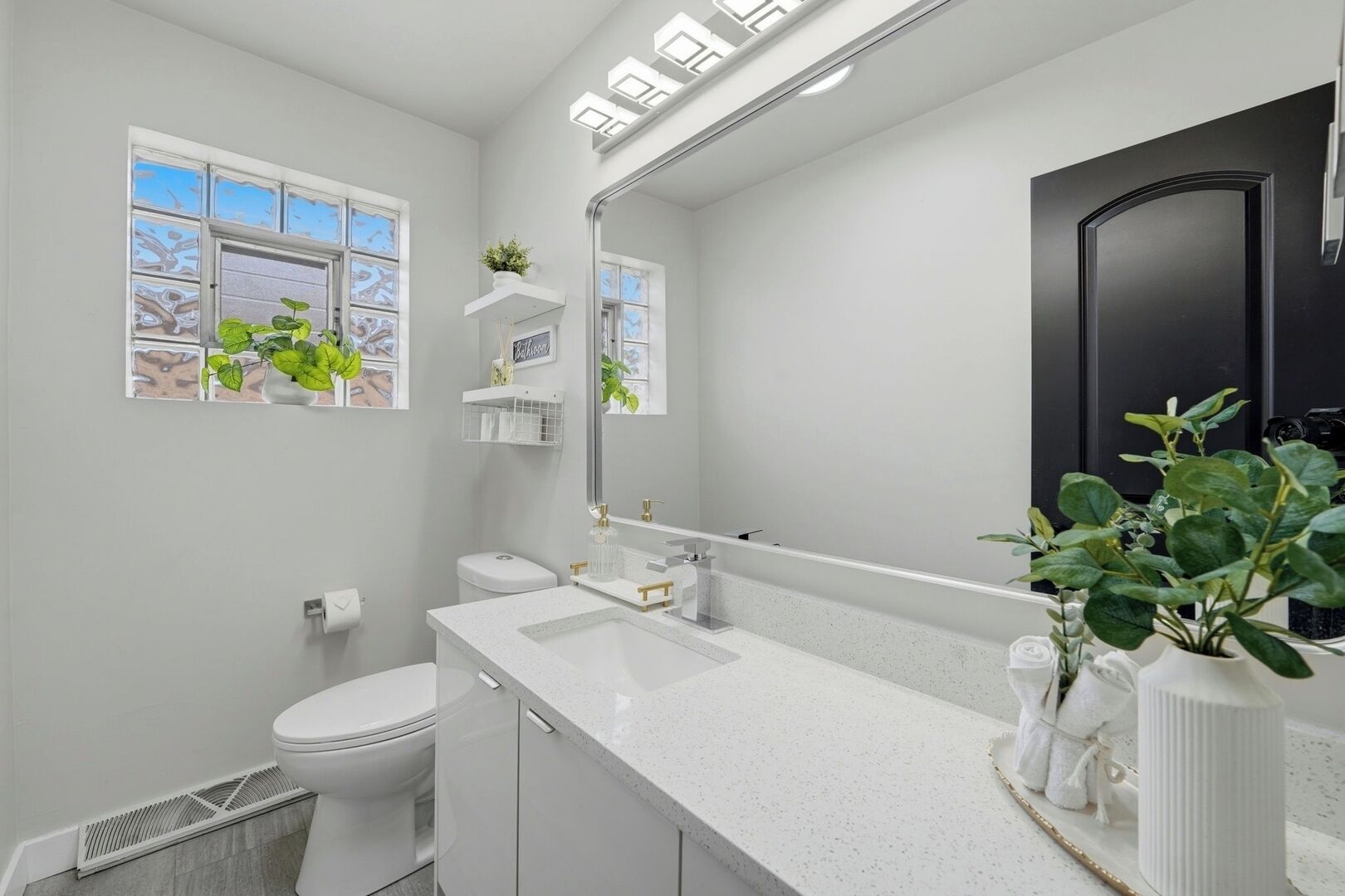 A modern bathroom with a white countertop, a large mirror, and a black door.