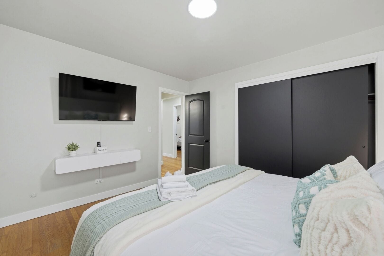 A modern bedroom with a bed, a TV mounted on the wall, a bedside table with a plant, and a wardrobe.
