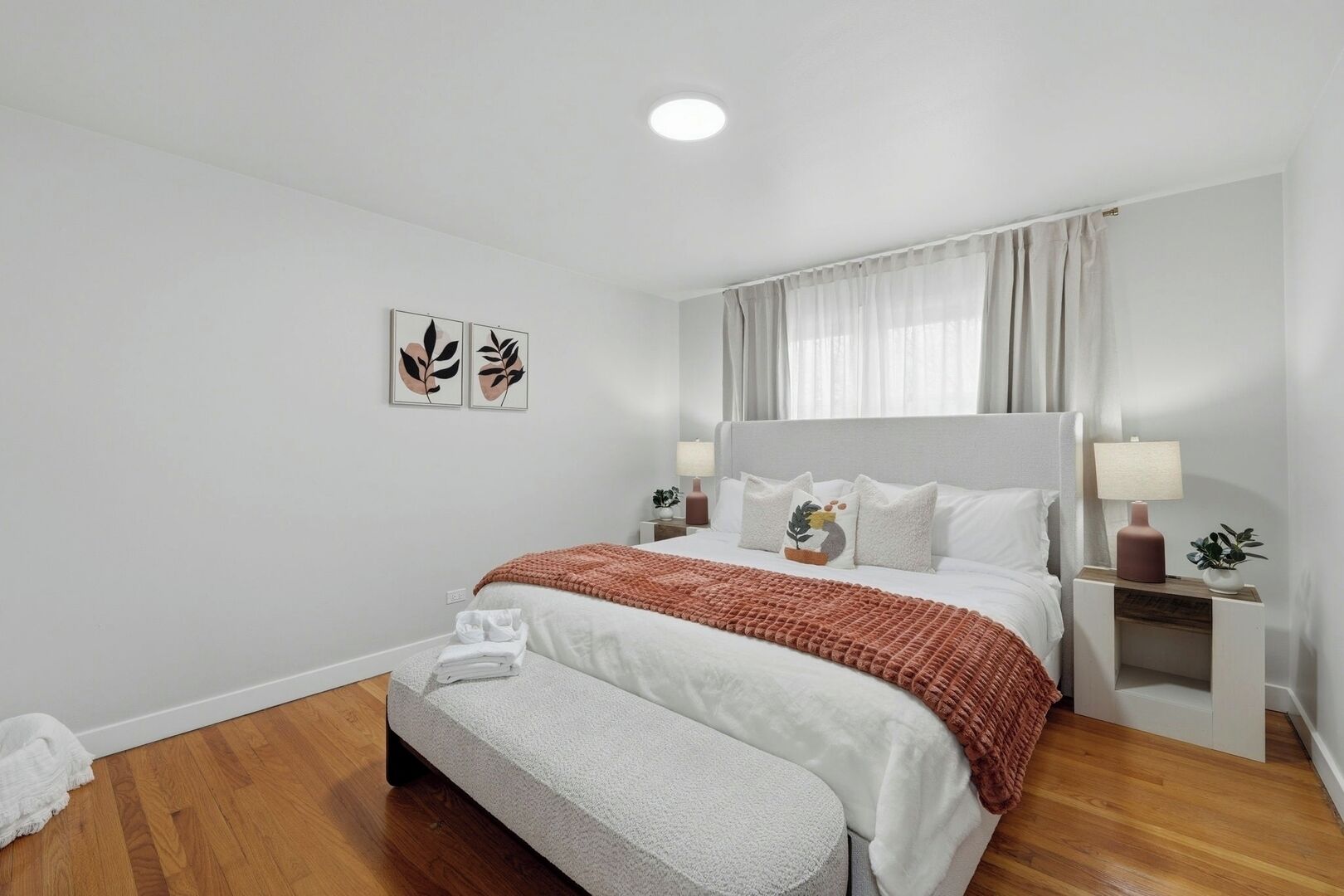 A bedroom with a large bed, bedside tables, a bench, and artwork on the wall.