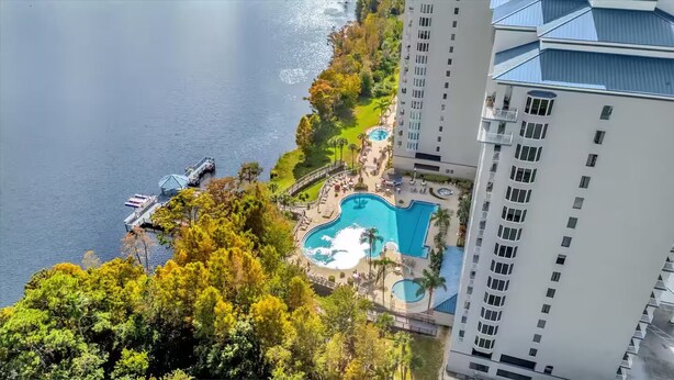 Um hotel alto com piscina, rodeado por vegetação exuberante e um cais que se projeta sobre a água.