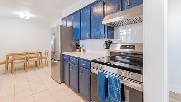 Een moderne keuken met blauwe kastjes, roestvrijstalen apparatuur en een houten eettafel.