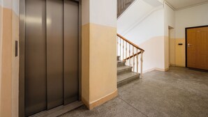 Ein Flur mit einem geschlossenen Aufzug, einer Treppe mit Holzhandlauf und einer Tür mit einer Nummer.