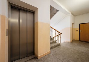 Ein Flur mit einem geschlossenen Aufzug, einer Treppe mit Holzhandlauf und einer Tür mit einer Nummer.