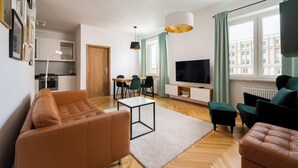 Ein modernes Wohnzimmer mit Sofa, Hocker, Fernseher und Essbereich.