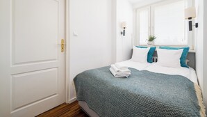 Une chambre à coucher avec un lit, une porte, une fenêtre avec des stores et une lampe fixée au mur.
