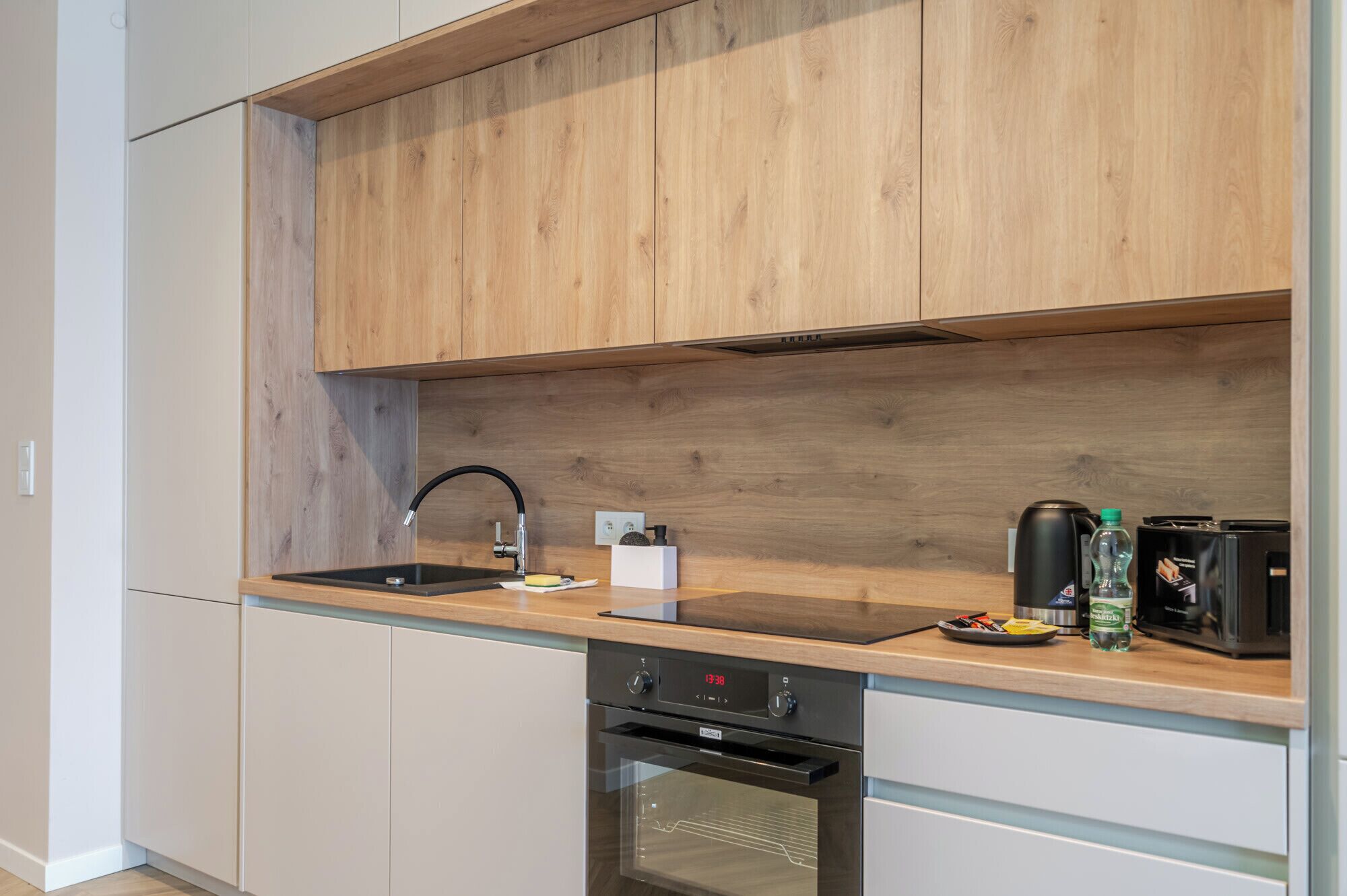 A modern kitchen with wooden cabinets, a stainless steel sink, a built-in oven, and a coffee maker.