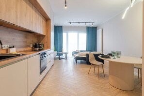 Eine moderne Küche mit Holzausstattung, ein Essbereich mit rundem Tisch und ein Bett mit Blick ins Freie.