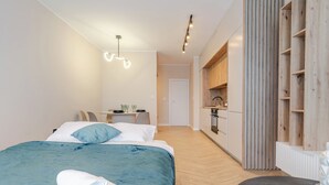Moderni hotellihuone, jossa on sänky, pieni pöytä tuoleineen, minikeittiö ja kylpyhuone, jossa on suihku.