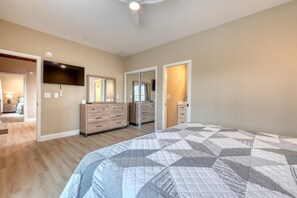 A bedroom with a large bed, a dresser, a TV, and a mirror. - Mossy Oaks Heights - Outdoor Kitchen (Hiawassee)
