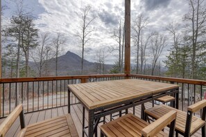 A wooden deck with a table and chairs, overlooking a mountainous landscape. - Mossy Oaks Heights - Outdoor Kitchen (Hiawassee)