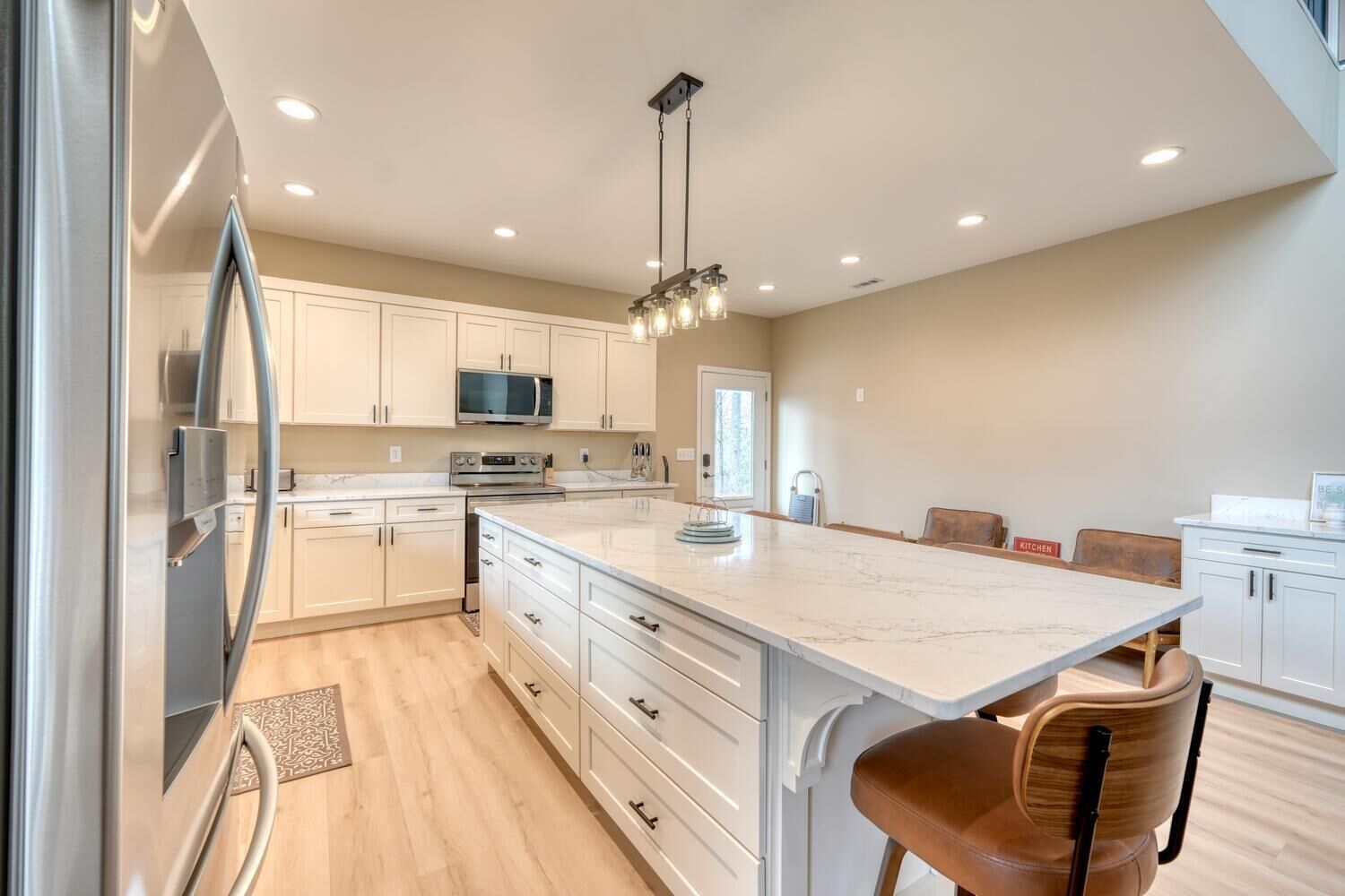 A modern kitchen with white cabinets, a large island, stainless steel appliances, and a pendant light.