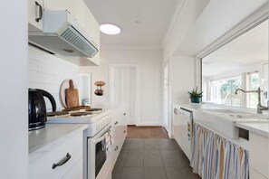A modern kitchen with white cabinetry, a stove, a kettle, and a sink.