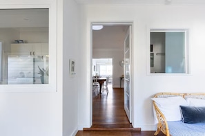 A hallway with a wooden floor leading to a dining area and a bedroom with a bed and a window.