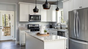 A modern kitchen with white cabinets, stainless steel appliances, and pendant lighting. - Modern Westside Retreat | 5 Min to Blue Ridge Parkway | 15 Min to Biltmore & Downtown Asheville (Fairview)