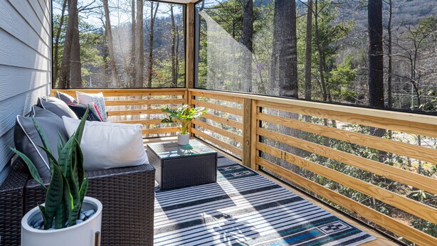 A balcony with a wicker sofa, cushions, a potted plant, and a patterned rug. - Modern Westside Retreat | 5 Min to Blue Ridge Parkway | 15 Min to Biltmore & Downtown Asheville (Fairview)