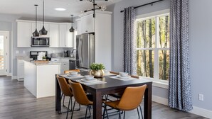 A modern kitchen with white cabinets, stainless steel appliances, and a dining area with a dark wooden table and orange chairs. - Modern Westside Retreat | 5 Min to Blue Ridge Parkway | 15 Min to Biltmore & Downtown Asheville (Fairview)