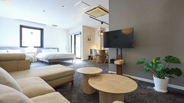 A modern hotel room with a large bed, two sofas, a TV, and a dining area.
